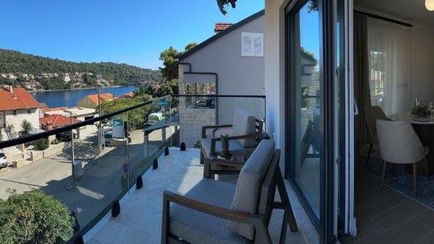 Een balkon met vrij uitzicht op een meer en huizen, ingericht met een stoel en een tafeltje.