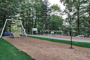 Un parc équipé d’une aire de jeux avec des balançoires, de bancs et d’un chemin piétonnier dallé.