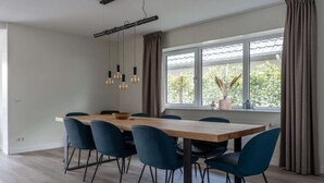 Un coin repas avec une table en bois et des chaises bleues, un luminaire suspendu et une fenêtre avec des rideaux.