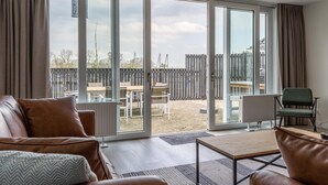 Un salon moderne doté d’une grande porte-fenêtre coulissante donnant sur un jardin avec une terrasse en bois et du mobilier d’extérieur.