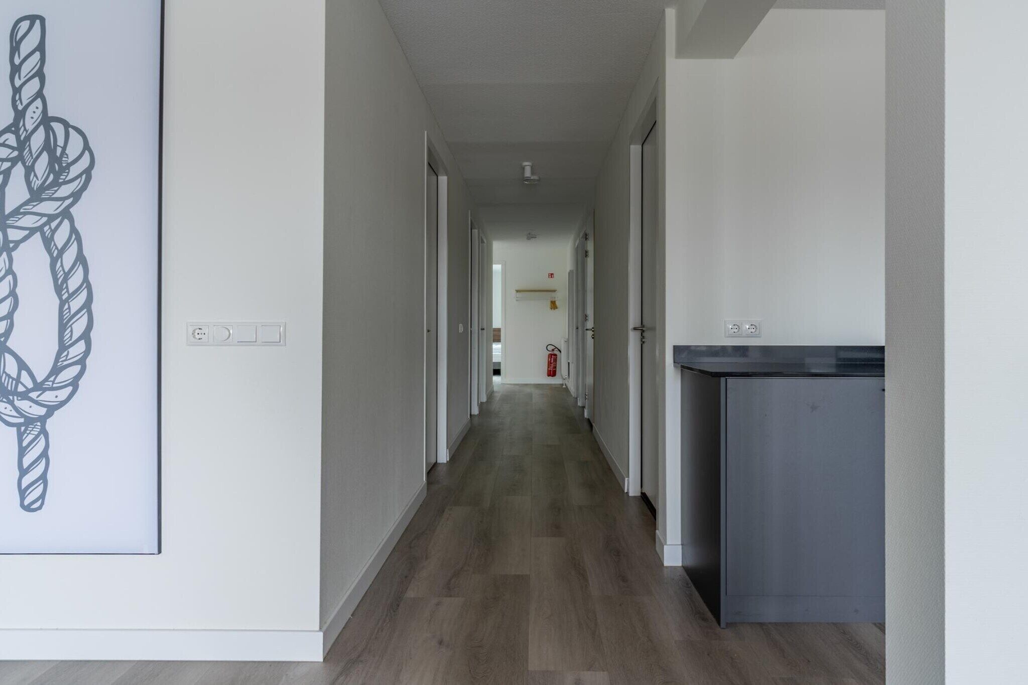 A hallway with a wooden floor, white walls, and a door at the end.