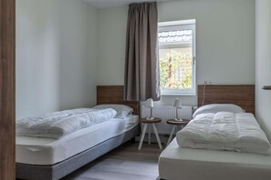 Una stanza con due letti, una finestra con tende, un tavolino e un termosifone.