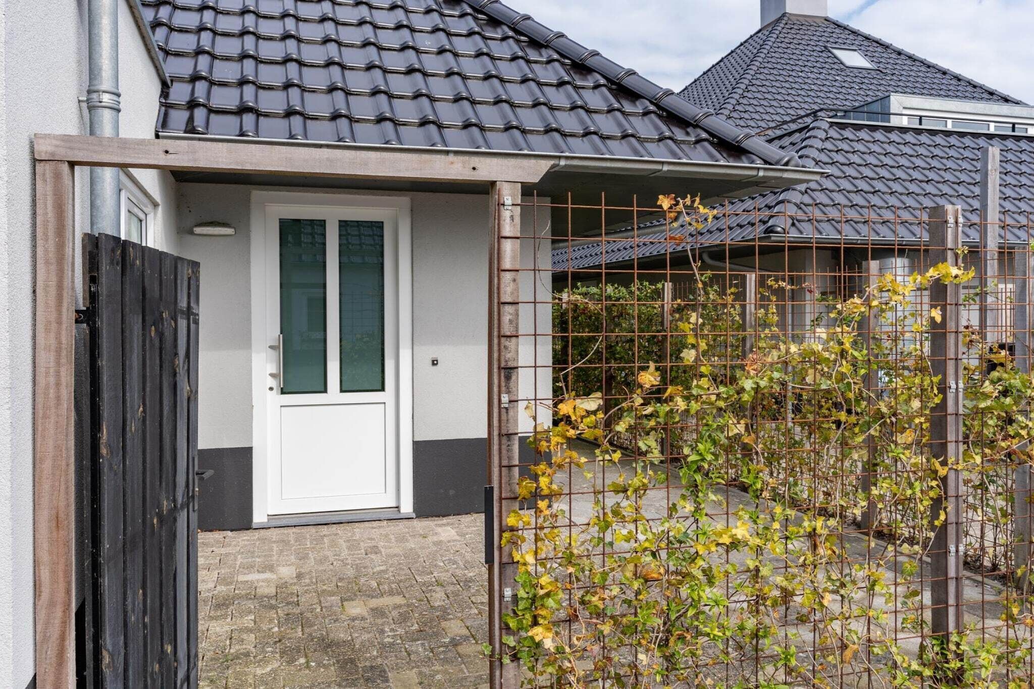 A house with a tiled roof, a white door, and a metal fence with climbing plants.