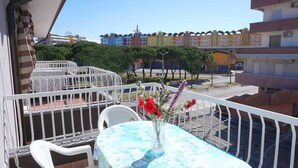 A balcony with a table and chairs, a vase with flowers, and a view of colorful buildings in the background. - Apartment in Caorle near Adriatic Beach (Caorle (VE))