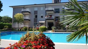A modern apartment building with a swimming pool, balconies, and lush landscaping. - Apartment in Caorle near Adriatic Beach (Caorle (VE))