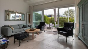 A modern living room with a grey sofa, a black leather ottoman, a round wooden coffee table, and two black armchairs. - Holiday Home in Nieuwvliet near the Beach (Nieuwvliet)