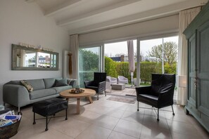 A modern living room with a grey sofa, a black leather ottoman, a round wooden coffee table, and two black armchairs. - Holiday Home in Nieuwvliet near the Beach (Nieuwvliet)