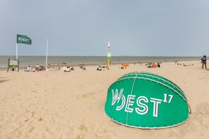A beach with a green inflatable structure labeled 'WEST17' and a flagpole with a flag.
