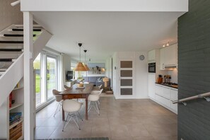 A modern kitchen with white cabinets, a dining area with a wooden table and chairs, and a staircase leading to another level.