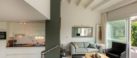 Una cocina moderna con armarios blancos, un comedor con una mesa redonda y una sala de estar con un sofá y una silla negra.