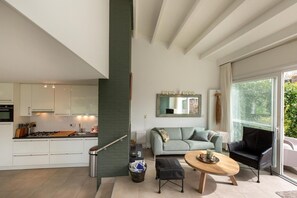 Una cocina moderna con armarios blancos, un comedor con una mesa redonda y una sala de estar con un sofá y una silla negra.