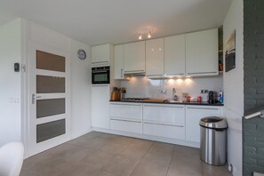 A modern kitchen with white cabinets, a stainless steel trash bin, and a clock on the wall.