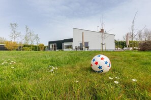 A modern building with a flat roof and large windows, surrounded by a grassy area with a sports ball.