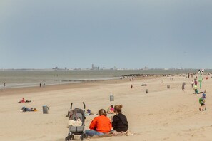 A beach with people, a stroller, and a cityscape in the distance. - Holiday Home in Nieuwvliet near the Beach (Nieuwvliet)