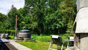 Eine Terrasse mit einem Steingrill, einer Holzbank und einem Metallstuhl.