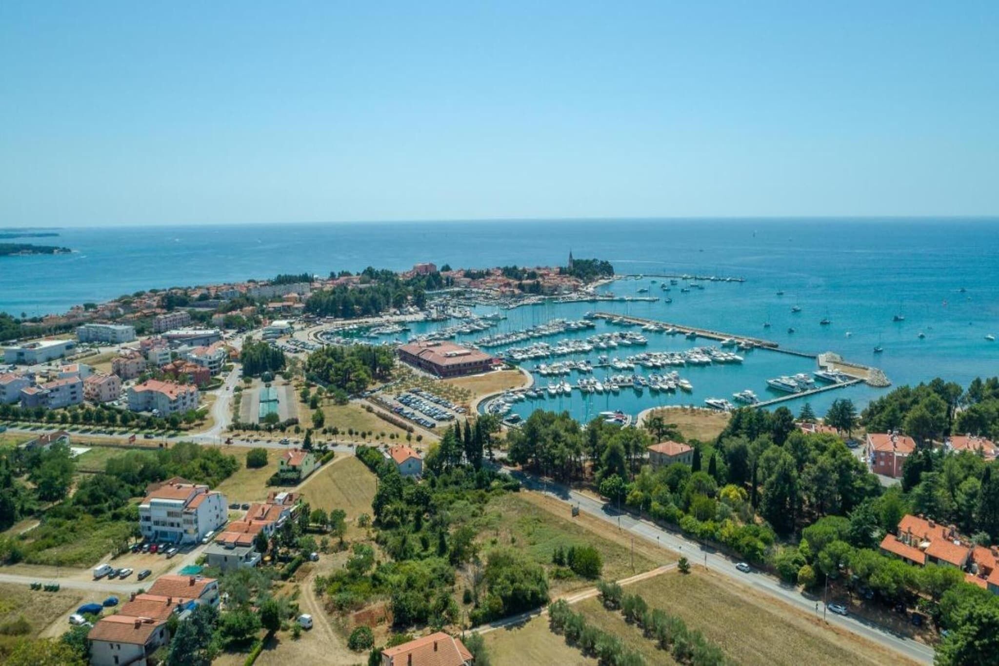 Vue aérienne d’une ville côtière avec un port de plaisance, des immeubles résidentiels et un ciel bleu dégagé.