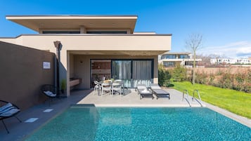 A modern pool area with a clear pool, lounge chairs, and a patio with a table and chairs.