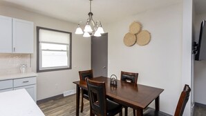 A dining area with a wooden table and chairs, a chandelier, a window, and a wall-mounted decorative item. - Ankeny Heights - A 4 bedroom and 2 bath home (Ankeny)