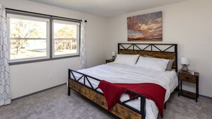 A bedroom with a bed, a nightstand, a lamp, a window with curtains, and a painting on the wall. - Ankeny Heights - A 4 bedroom and 2 bath home (Ankeny)