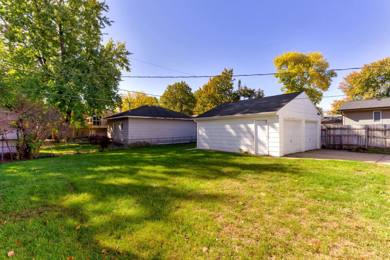 A residential backyard with two white sheds, a grassy lawn, and trees.