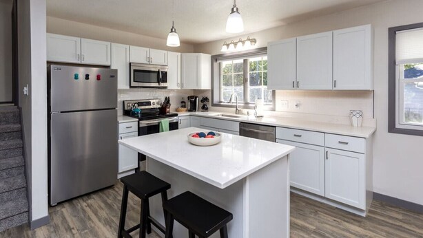 A modern kitchen with white cabinets, stainless steel appliances, and a central island with stools. - Ankeny Heights - A 4 bedroom and 2 bath home (Ankeny)
