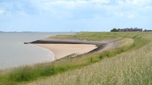 A coastal landscape with a sandy beach, grassy dunes, and a building in the background.