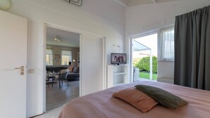 A bedroom with a large bed, a television on a stand, and a view of a garden through a window.