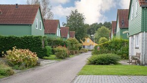 A row of green houses with red roofs, a paved path, and a bench.