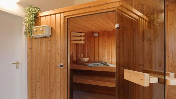 A wooden sauna with a glass door, wooden benches, and a shelf with towels.