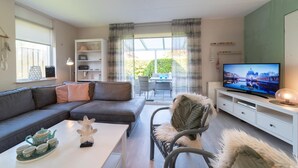 A modern living room with a sofa, coffee table, and TV. There is a balcony with a table and chairs.