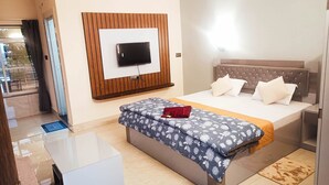 A modern hotel room with a large bed, a flat-screen TV mounted on a wooden panel, a bedside table, and a small desk. - Nature Green Resort (Mal)