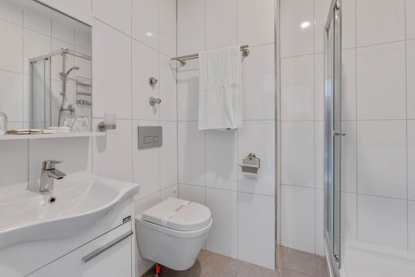 Une salle de bain moderne avec un lavabo blanc, des toilettes et une douche à parois de verre.