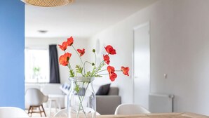 A dining table with a clear glass vase containing red flowers, white chairs, and a wooden table surface. - Holiday Home in Nes near Vleijen Area (Nes)