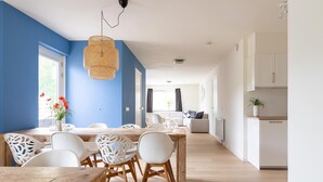 A modern living room with a dining area, featuring a blue accent wall, wooden flooring, and white furniture. - Holiday Home in Nes near Vleijen Area (Nes)