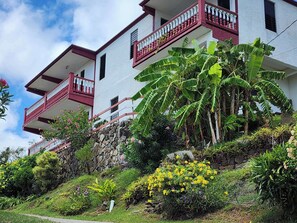 Un immeuble à plusieurs étages doté de balcons, entouré d’une végétation luxuriante et de plantes en fleurs.