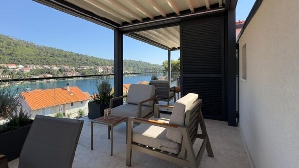 A balcony with outdoor furniture, a view of a river, and a hillside in the background.