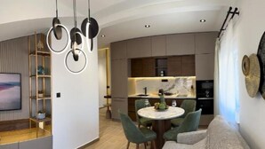 A modern living room with a curved sofa, a dining table with chairs, and a kitchen area with built-in cabinets and a marble countertop.