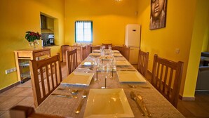 A long dining table set with plates, cutlery, and wine glasses, flanked by wooden chairs, in a room with yellow walls and a Buddha painting.