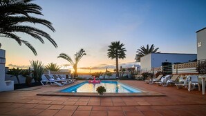 A swimming pool with lounge chairs and palm trees, surrounded by buildings.