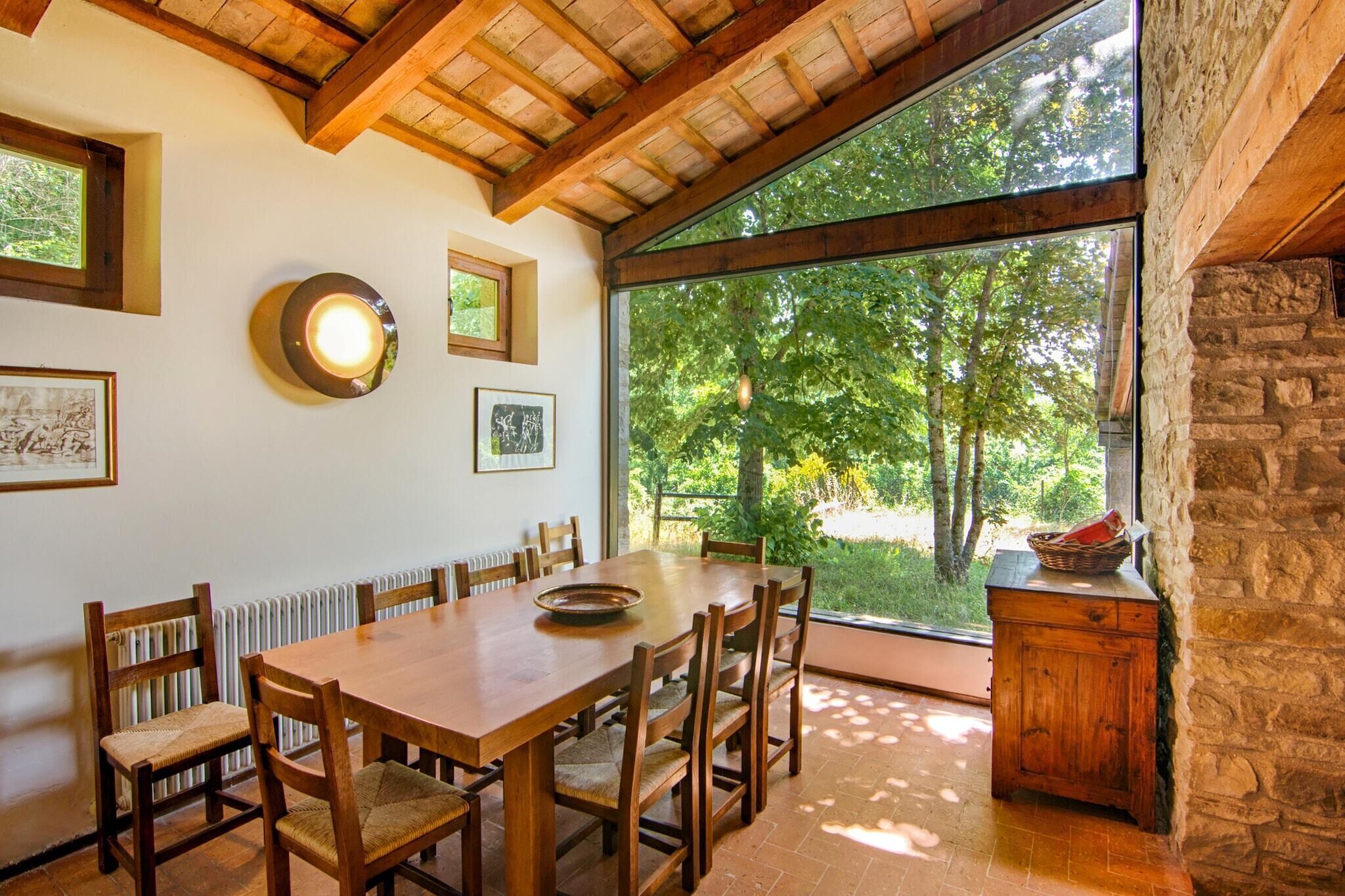 A dining area with a wooden table and chairs, large windows with a view of trees, and a stone wall.