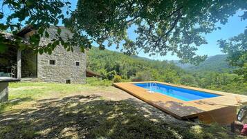 Un edificio de piedra con una terraza de madera y una piscina.