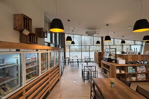 Ein geräumiges Café mit Holztischen, großen Fenstern und hängenden Pendelleuchten.