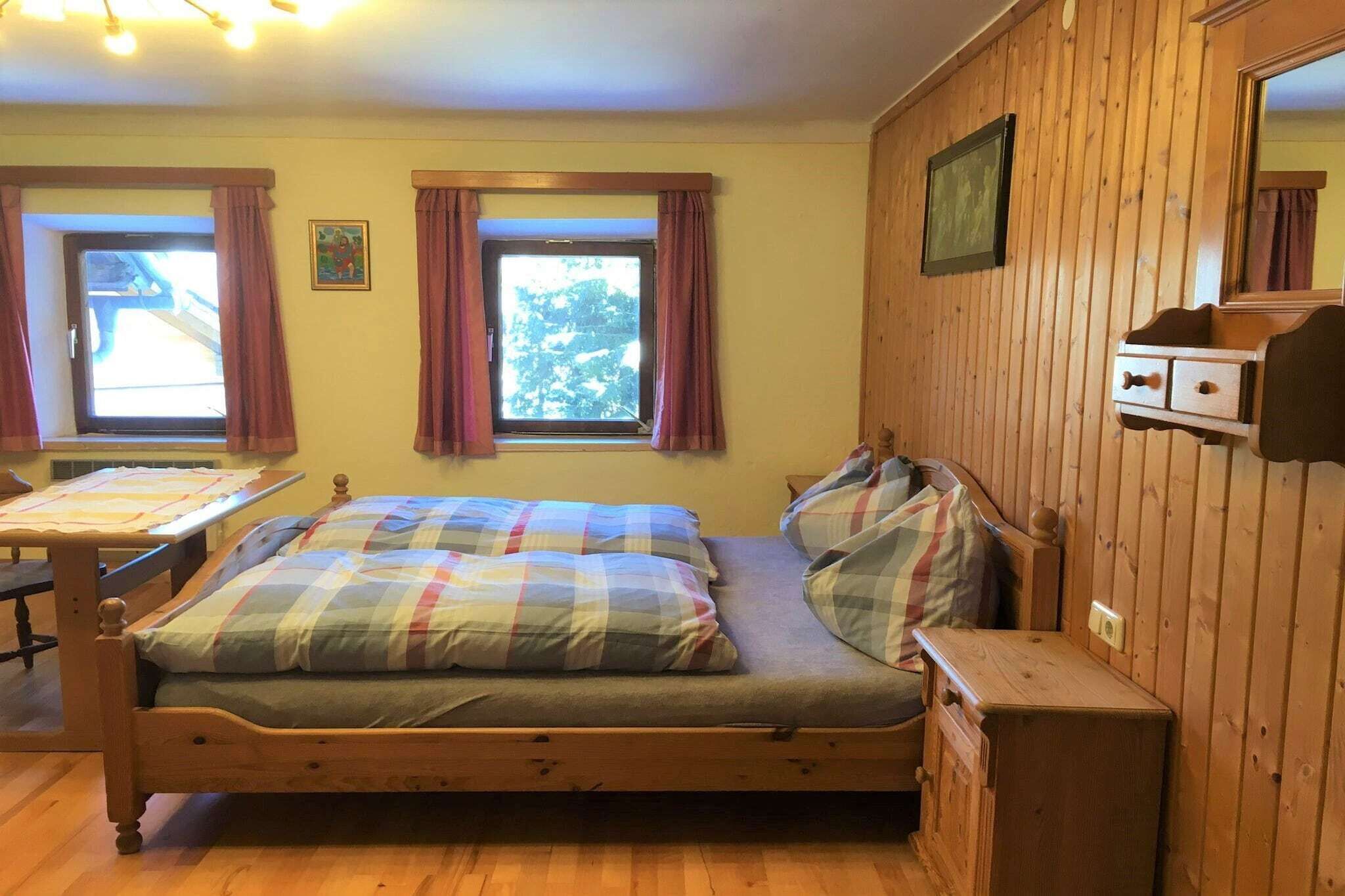 A wooden-paneled room with a bed, a small table, and a window with curtains.