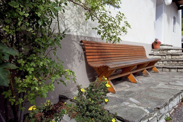 Un banco de madera contra una pared blanca, con una planta en maceta y flores amarillas cerca.