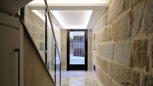 Un pasillo con paredes de piedra, barandilla de vidrio y puerta que da al exterior.