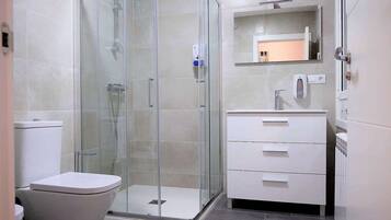 A modern bathroom with a glass-enclosed shower, a white toilet, and a vanity with a mirror.