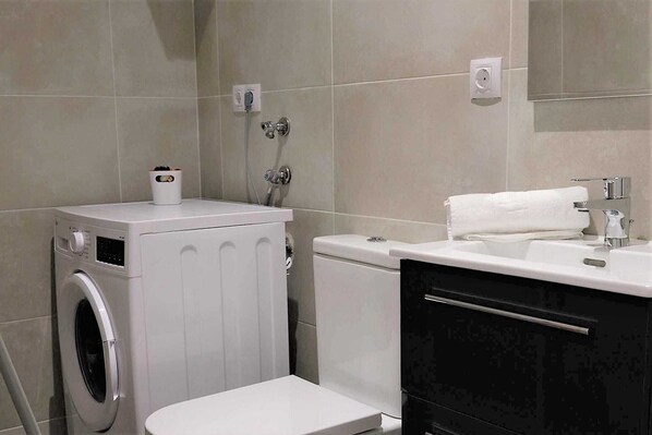 Un baño pequeño con lavadora, inodoro y lavabo.