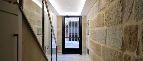 A hallway with stone walls, a glass railing, and a door leading outside.