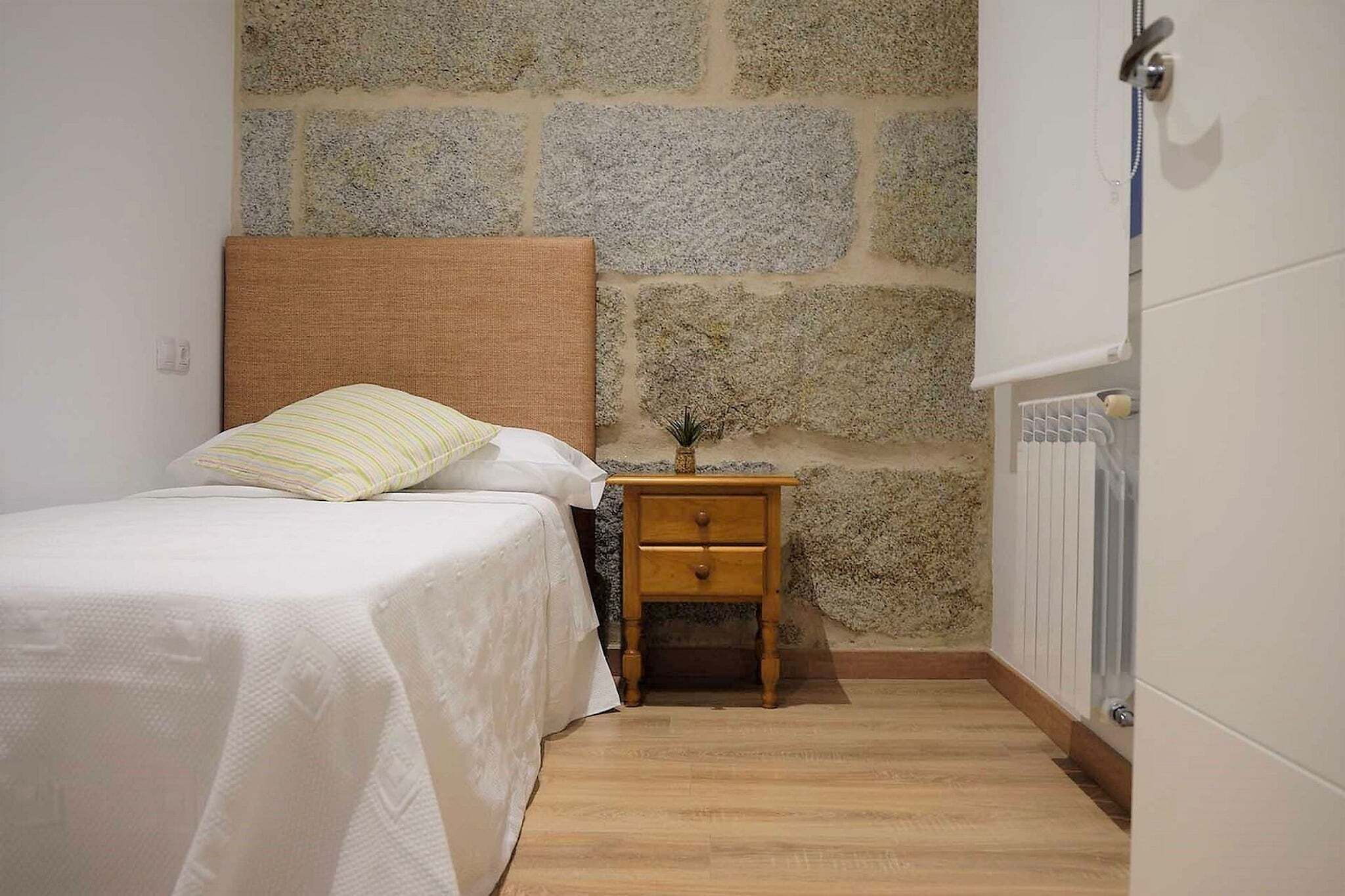 Una camera da letto piccola e ordinata con un letto, un comodino e un muro in pietra.