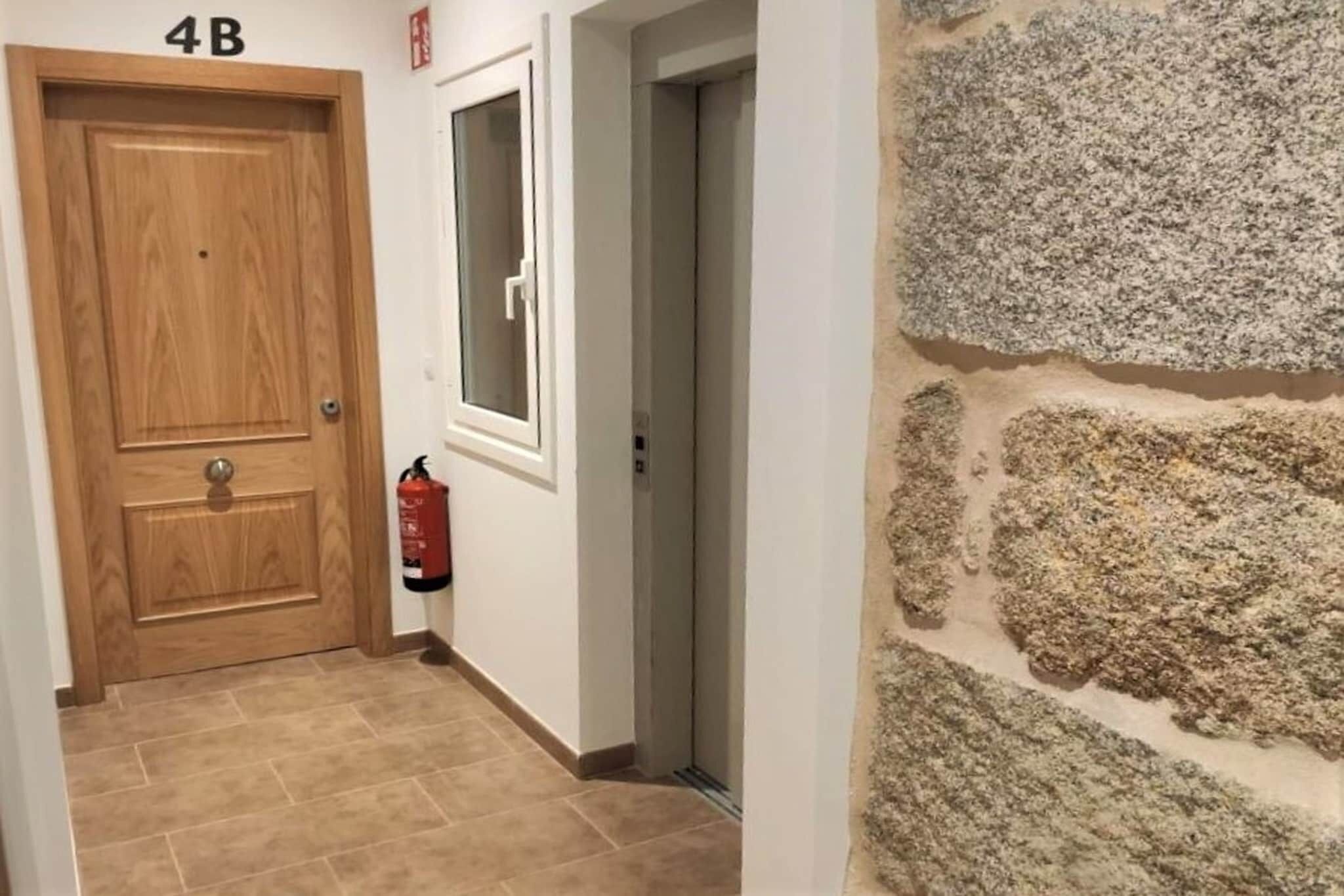 Un pasillo con una puerta de madera con la leyenda “4B”, un extintor y una pared de piedra.